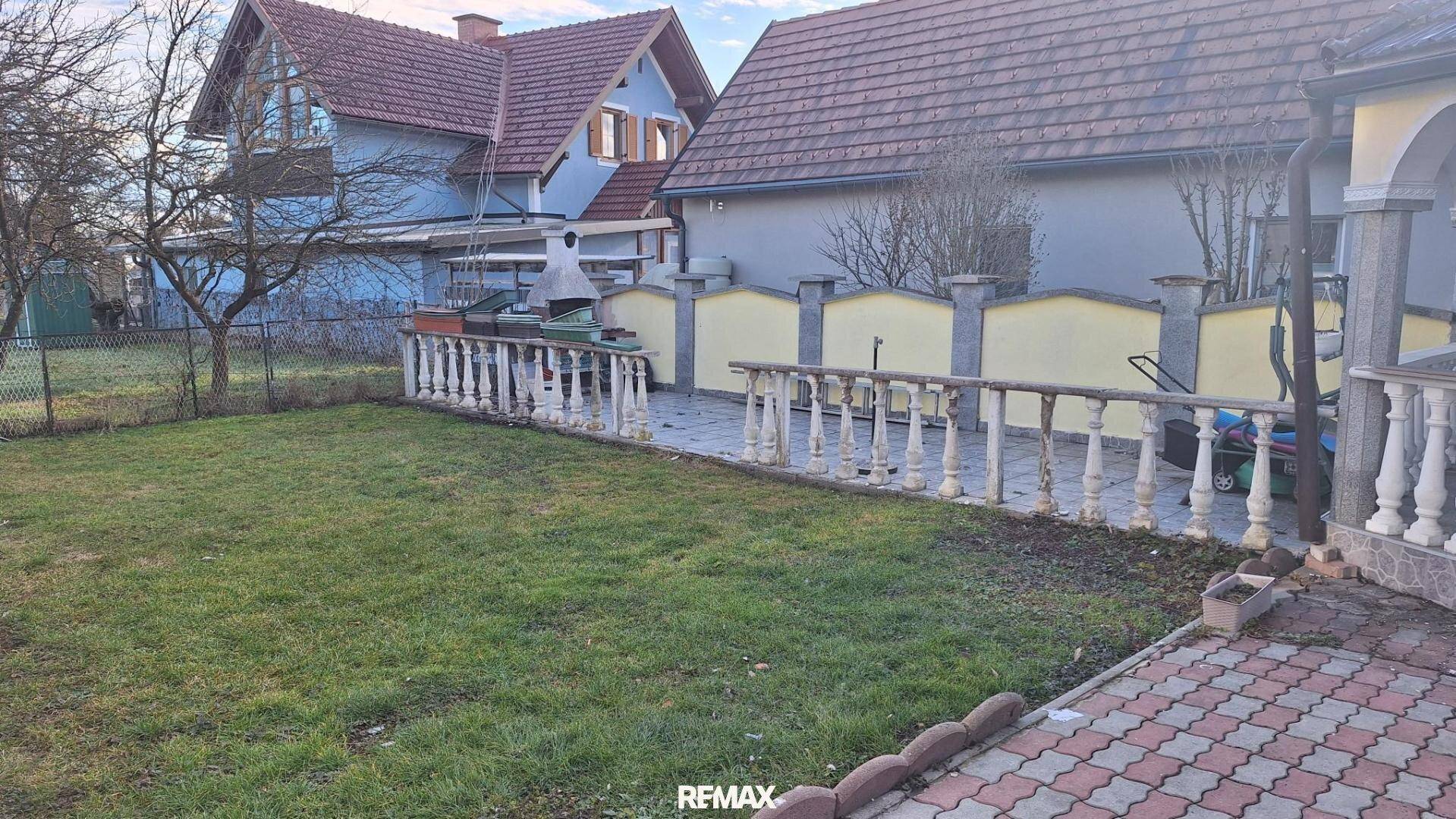Rasenfläche mit gepflastertem Weg, niedriger Balustrade und weiteren Häusern im Hintergrund.