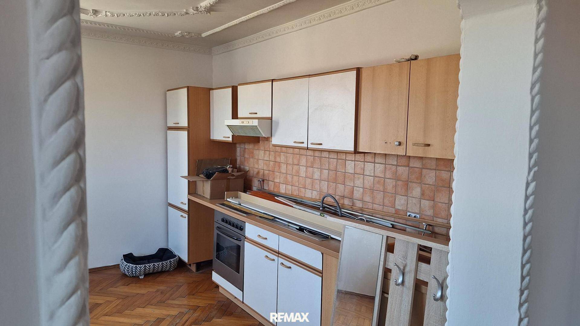 Ältere Küche mit Holzschränken, weißen Fronten, Fliesenrückwand und Fischgrätparkett.