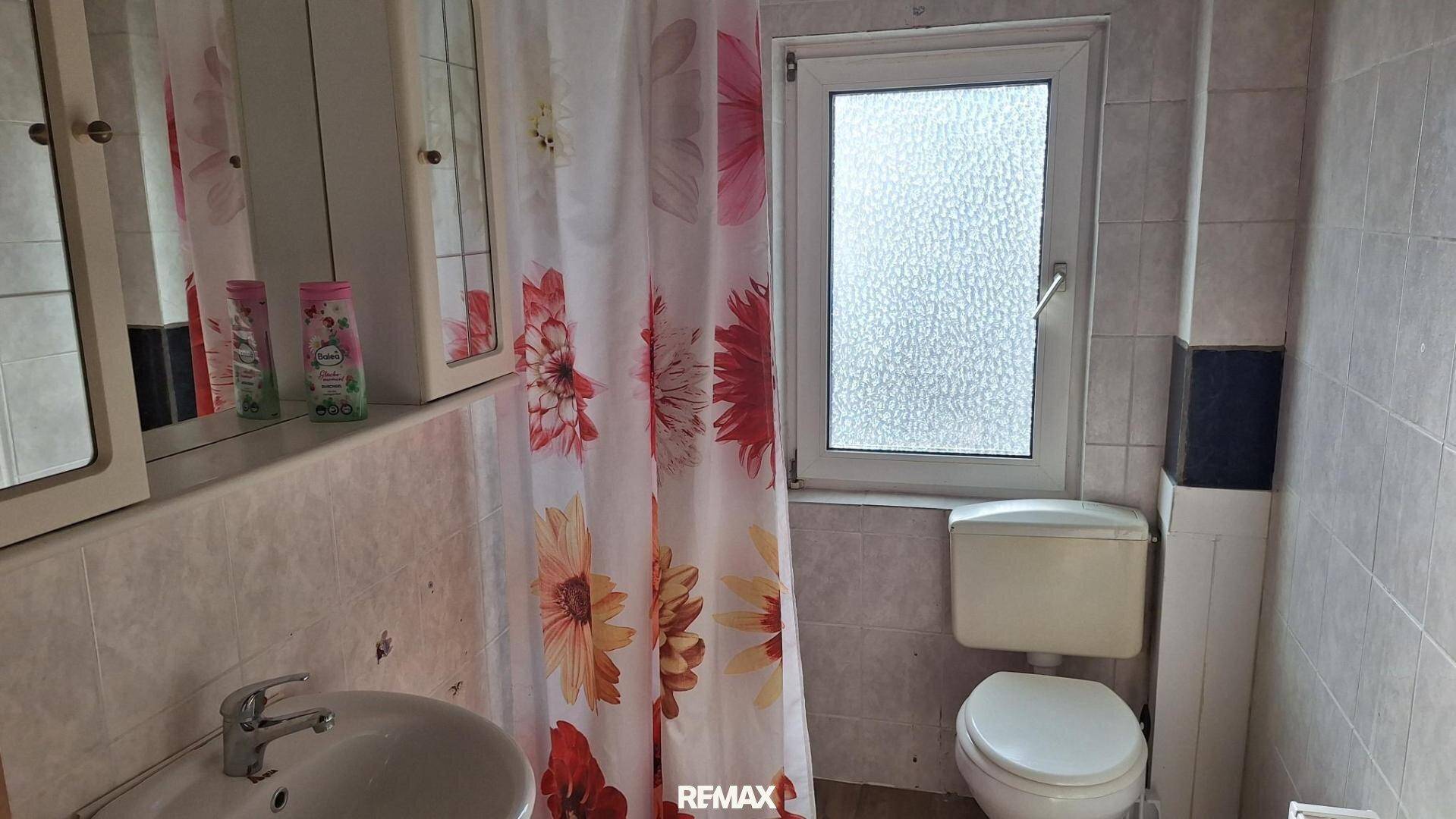 Kleines Badezimmer mit Toilette, Waschbecken, Spiegelschrank und Fenster.