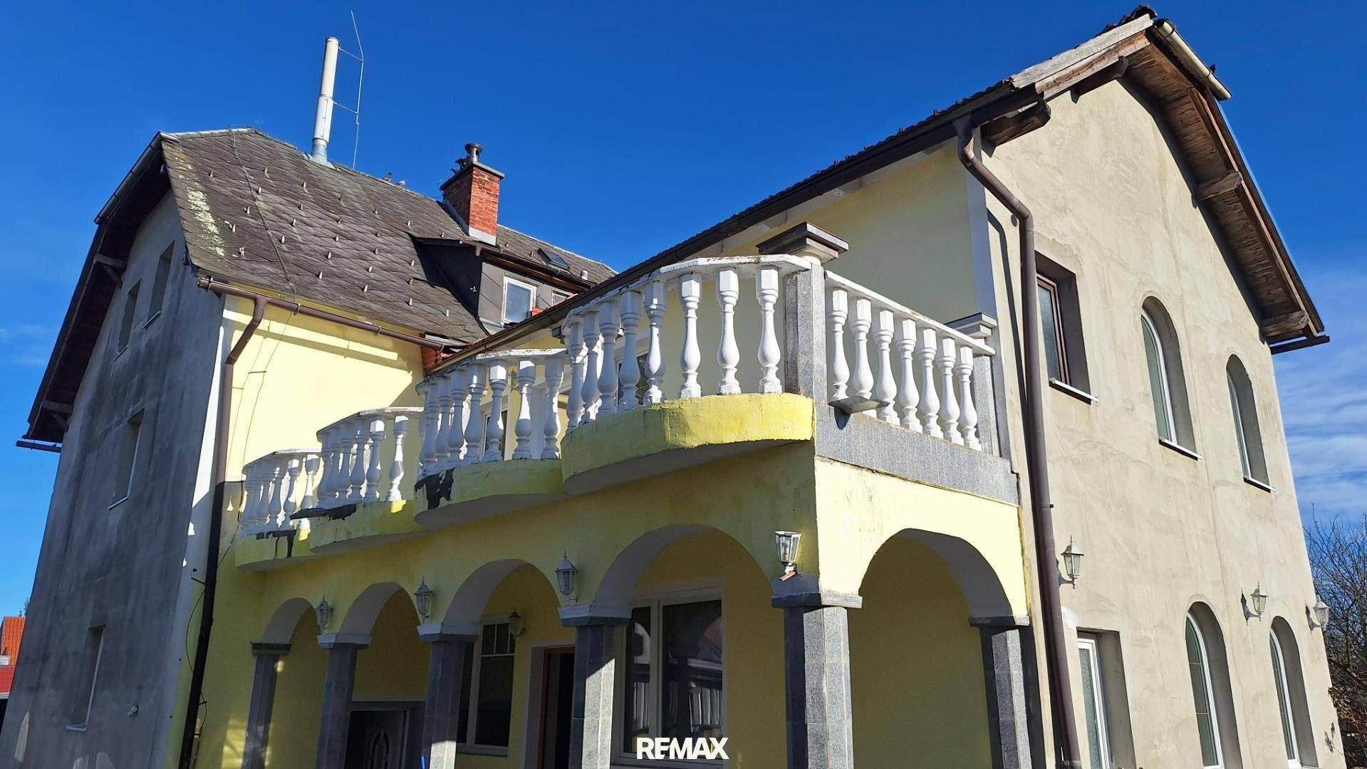 Fassade des Gebäudes mit mehreren Balkonen, Balustraden und Rundbogenfenstern im Erdgeschoss.