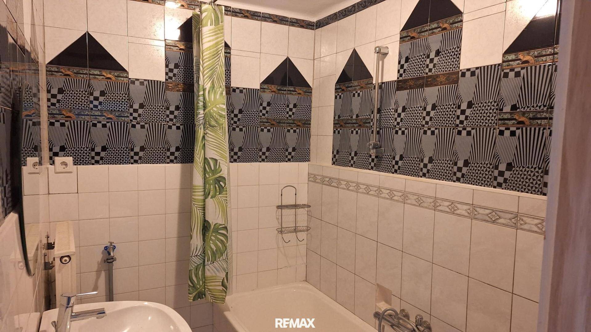 Badezimmer mit weißen und gemusterten Fliesen, Waschbecken und Badewanne mit Duschvorhang.