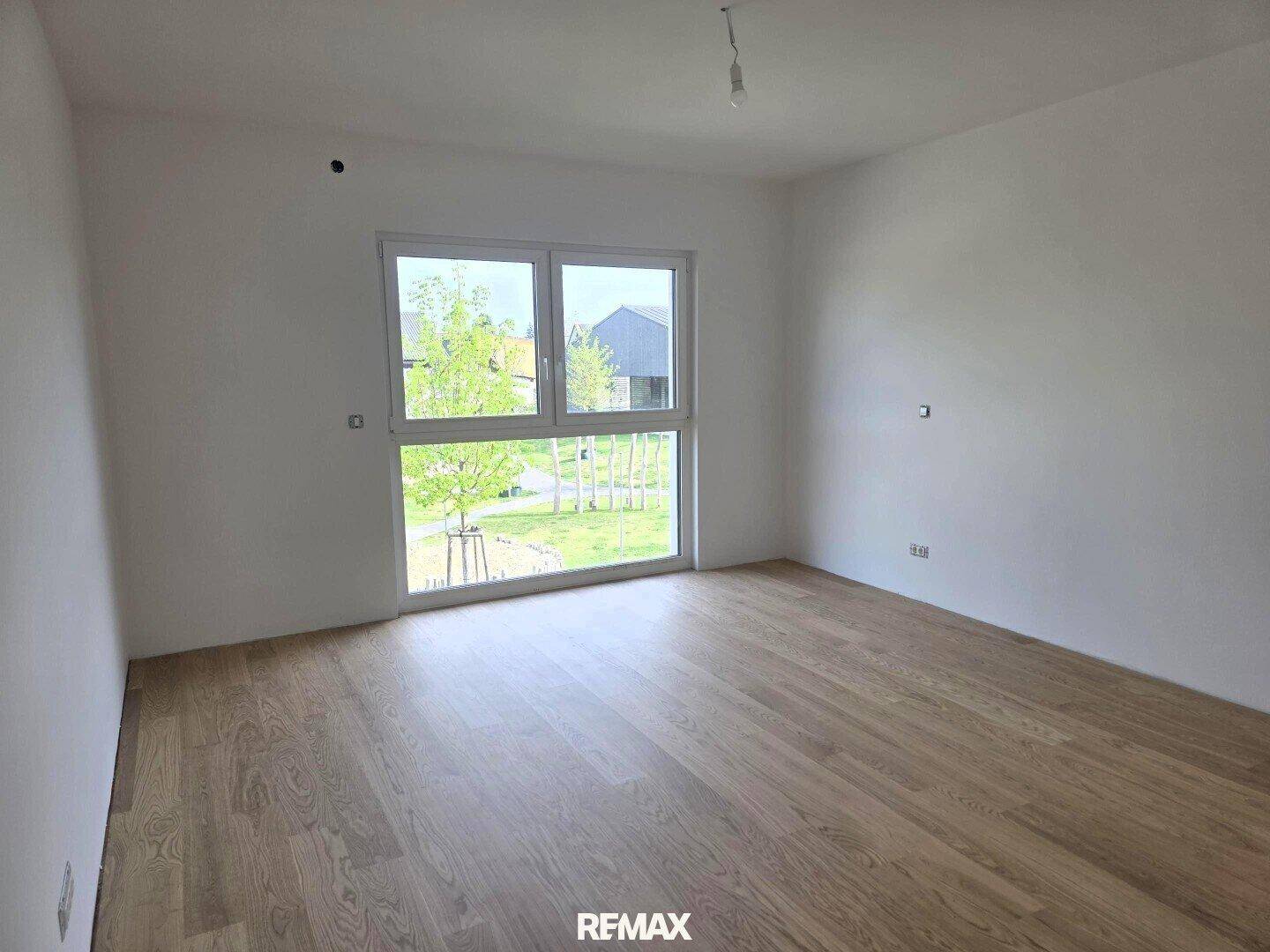 Helles Schlafzimmer mit großem Fenster und Blick ins Grüne, ausgestattet mit Parkettboden.