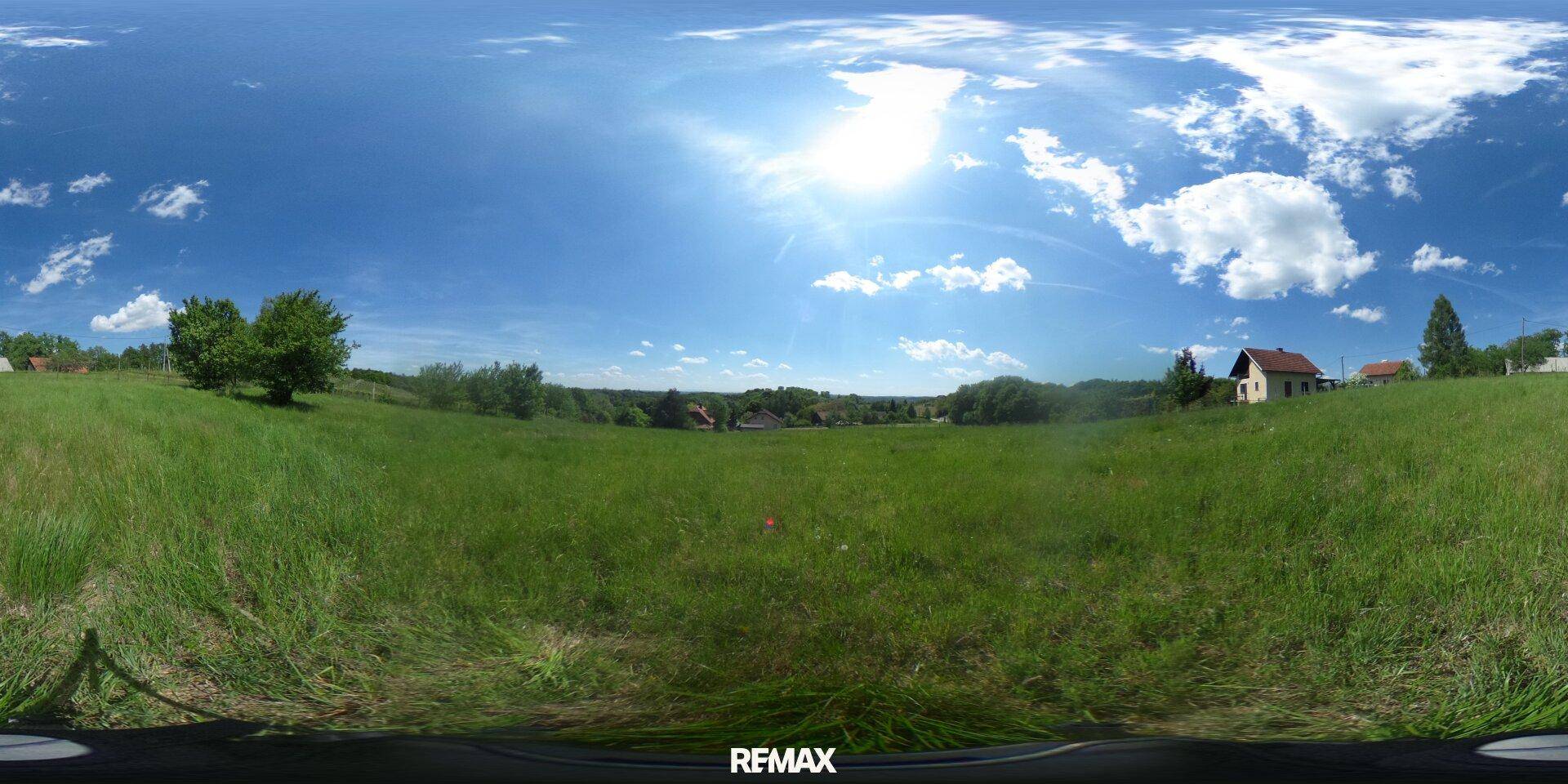 Weitläufige grüne Landschaft unter blauem Himmel mit vereinzelten Häusern und Bäumen am Horizont.