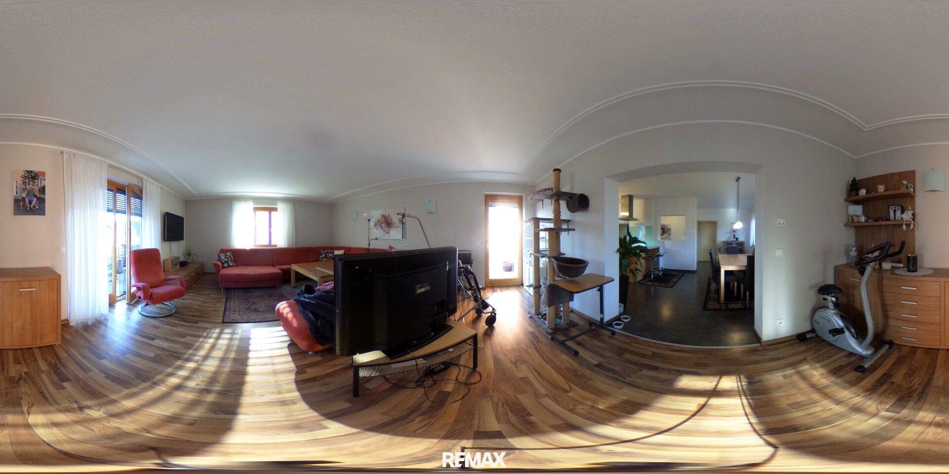 Helles Wohnzimmer mit Sofa, Fernseher und Zugang zu weiteren Wohnbereichen.