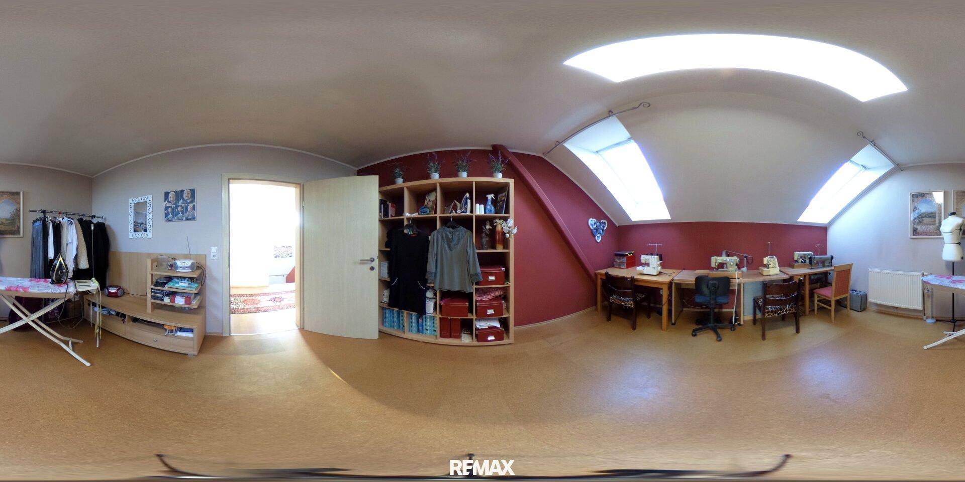Helles Arbeitszimmer mit Dachschrägen, Regalen und mehreren Arbeitsplätzen unter den Dachfenstern.