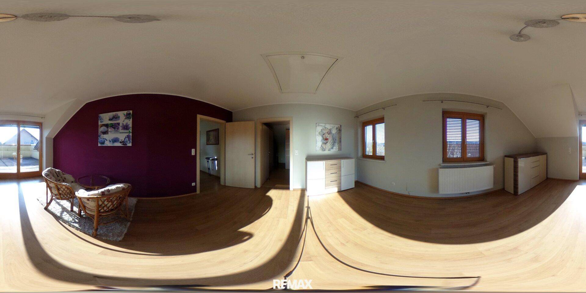 Gemütliches Wohnzimmer mit Holzboden, lila Akzentwand und Zugang zur Außenterrasse.