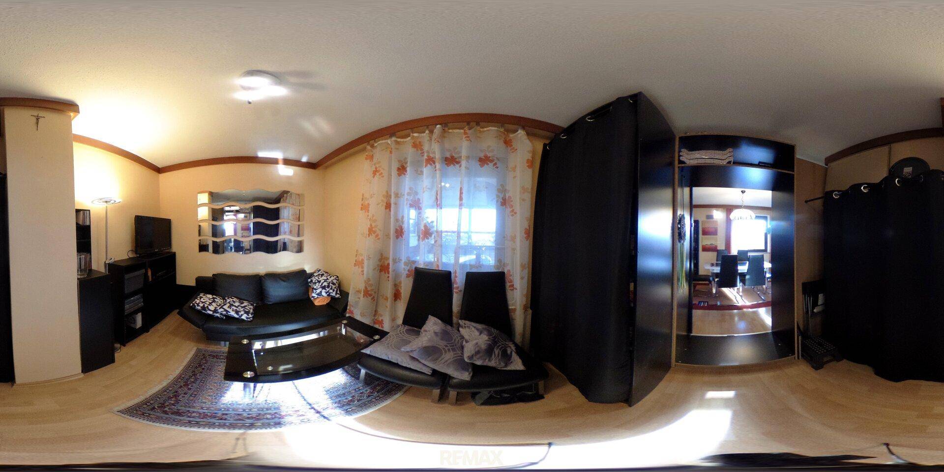 Gemütliches Wohnzimmer mit Holzboden, dunklen Sofas und großen Fenstern.