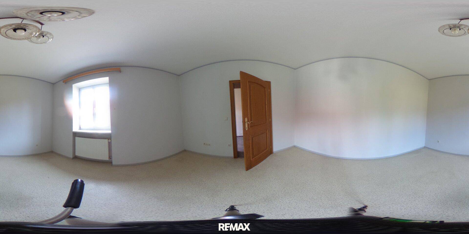 Leeres Schlafzimmer mit hellem Teppichboden, Fenster und Holztür, bereit zur individuellen Gestaltung.