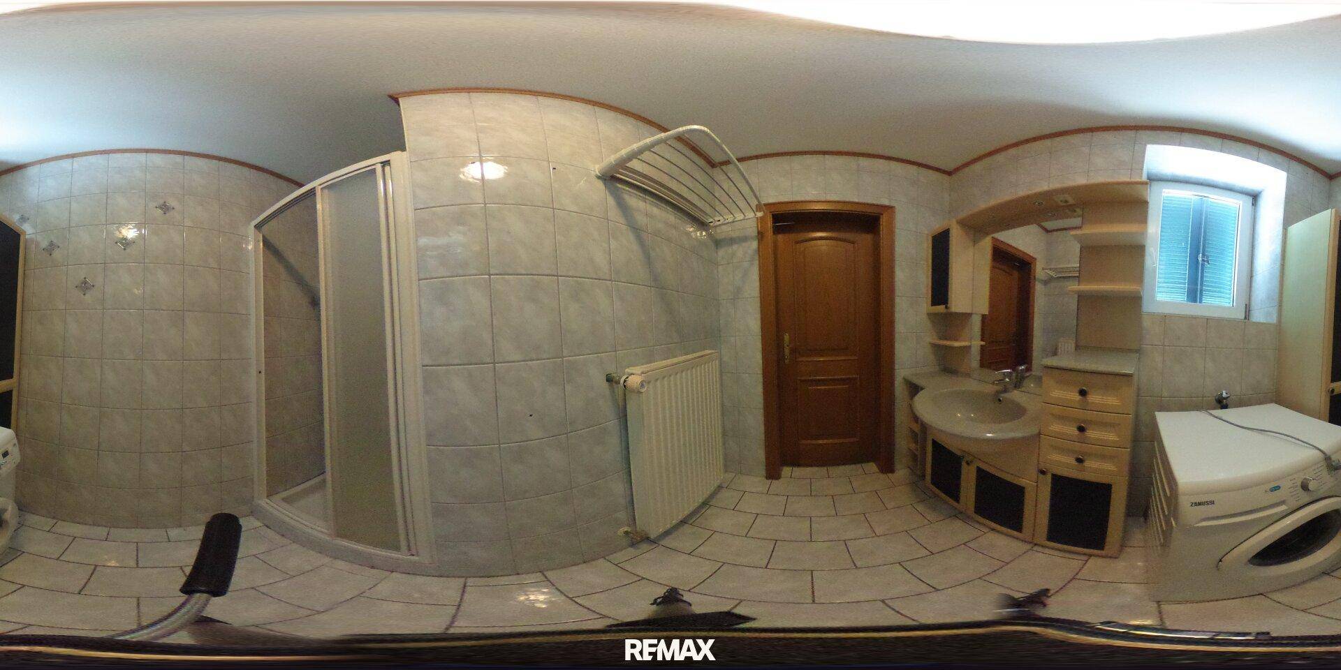 Gefliestes Badezimmer mit Duschkabine, Waschbeckenunterschrank und Waschmaschine, funktional eingerichtet.