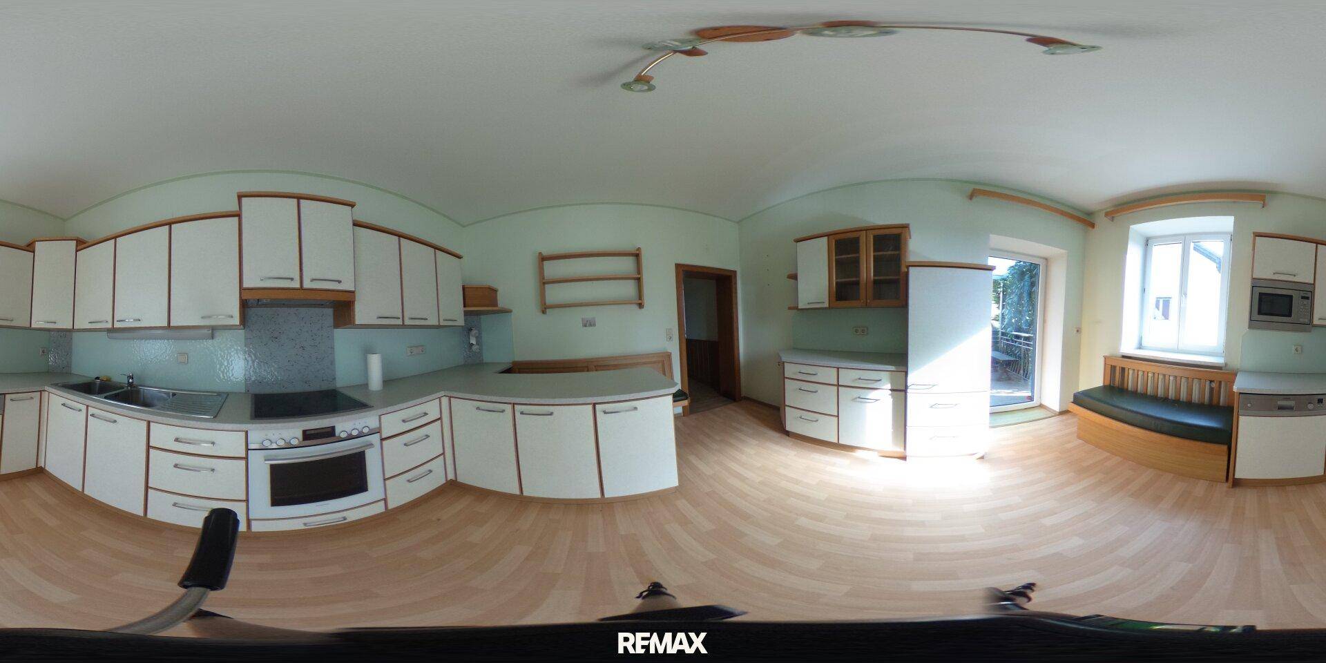 Panoramaansicht der Küche mit Einbauküche, Geräten und integrierter Sitzbank am Fenster.