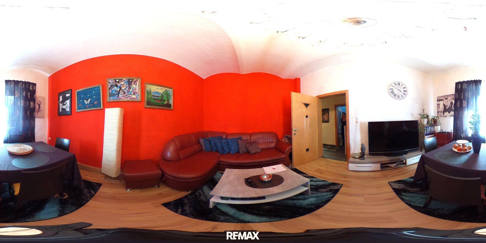 Gemütliches Wohnzimmer mit roter Akzentwand, Ledersofa und Holzboden für entspannte Stunden.
