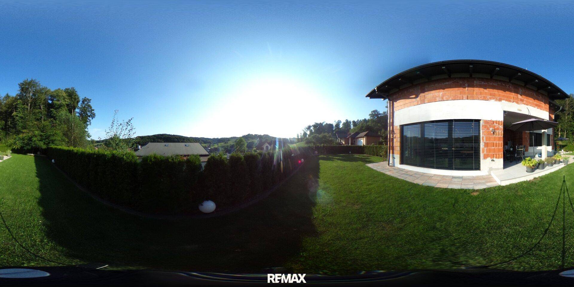 Sonnige Rasenfläche im Garten mit Hecken und Blick auf die umliegende Landschaft.