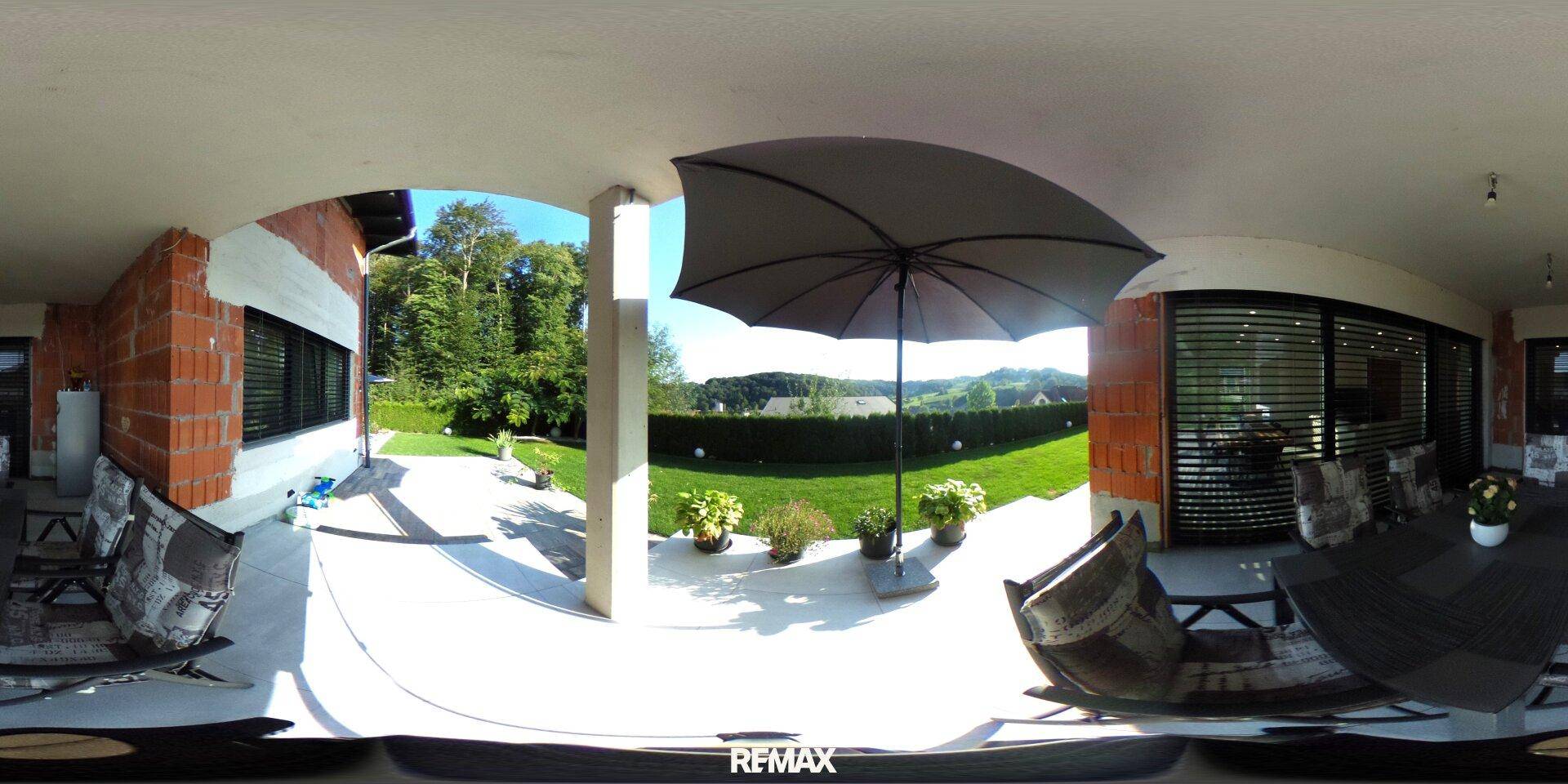 Überdachte Terrasse mit Sitzgelegenheiten und Blick auf den Garten und die weite Landschaft.