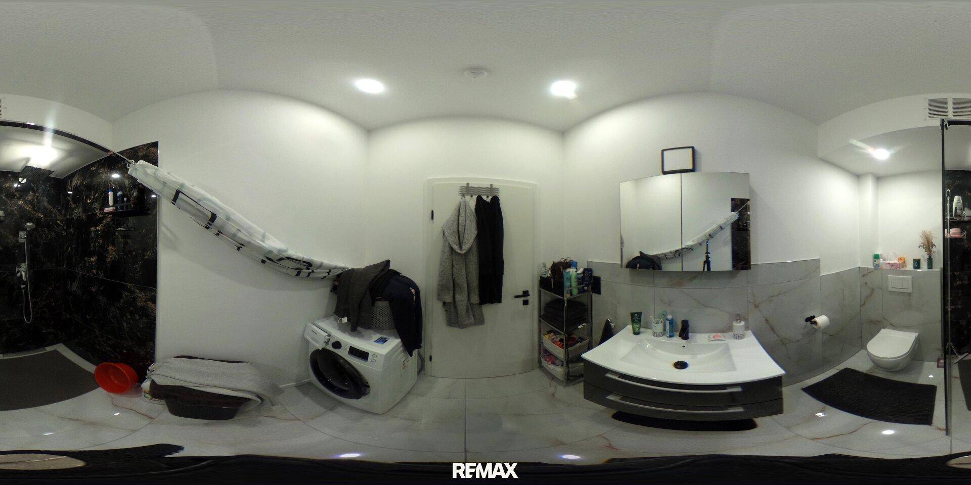 Modernes Badezimmer mit Dusche, WC, Waschbecken und Waschmaschine, ausgestattet mit dunklen und hellen Fliesen.