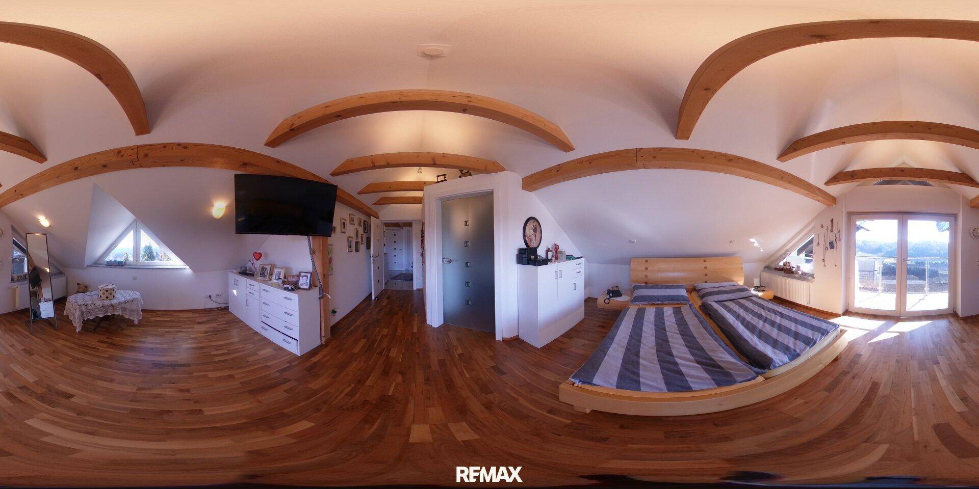 Großes Schlafzimmer mit Holzboden, freiliegenden Holzbalken und viel Tageslicht durch die Fenster.