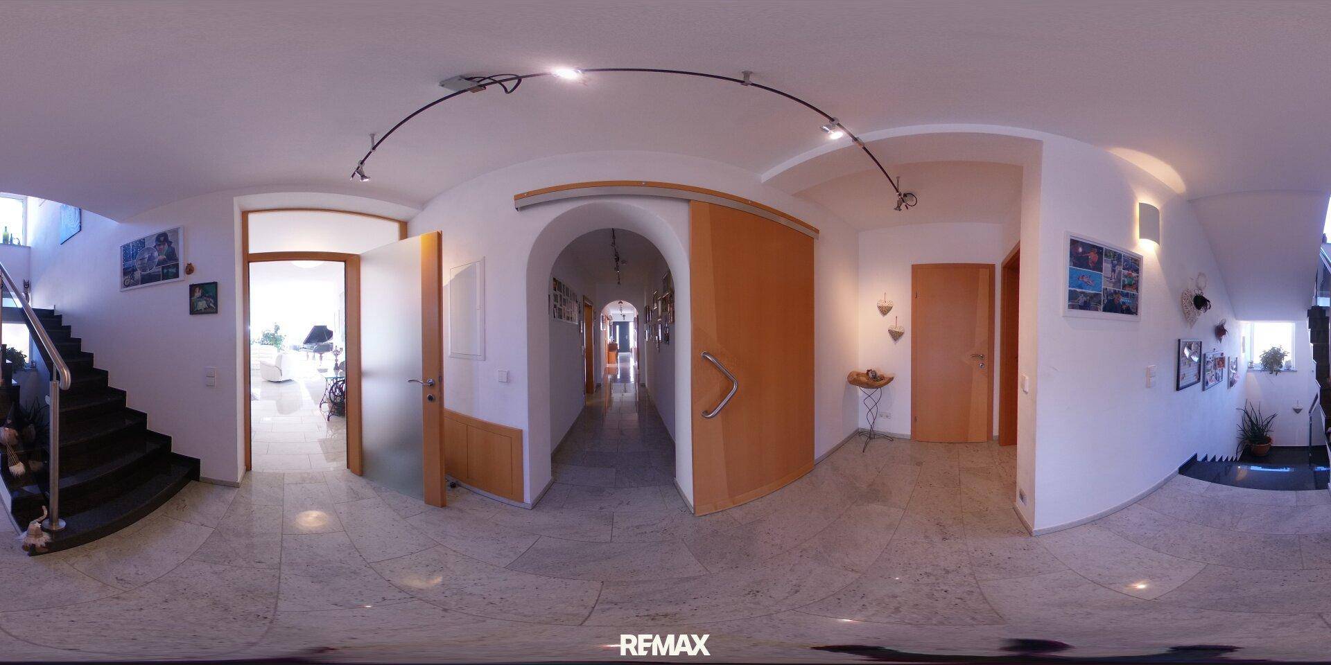 Heller Flur mit Fliesenboden und Holzdetails, der zu verschiedenen Räumen und Treppen führt.