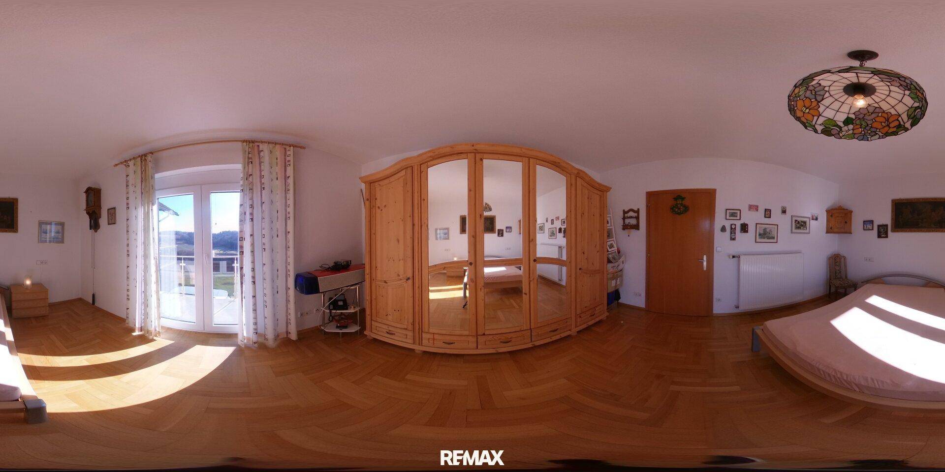 Schlafzimmer mit großem Holzschrank, Holzboden und Zugang zu einem Balkon durch Fenstertüren.