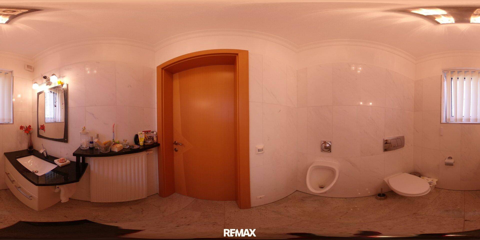 Badezimmer mit Waschbecken, Spiegel, Wand-WC und Urinal, komplett gefliest.
