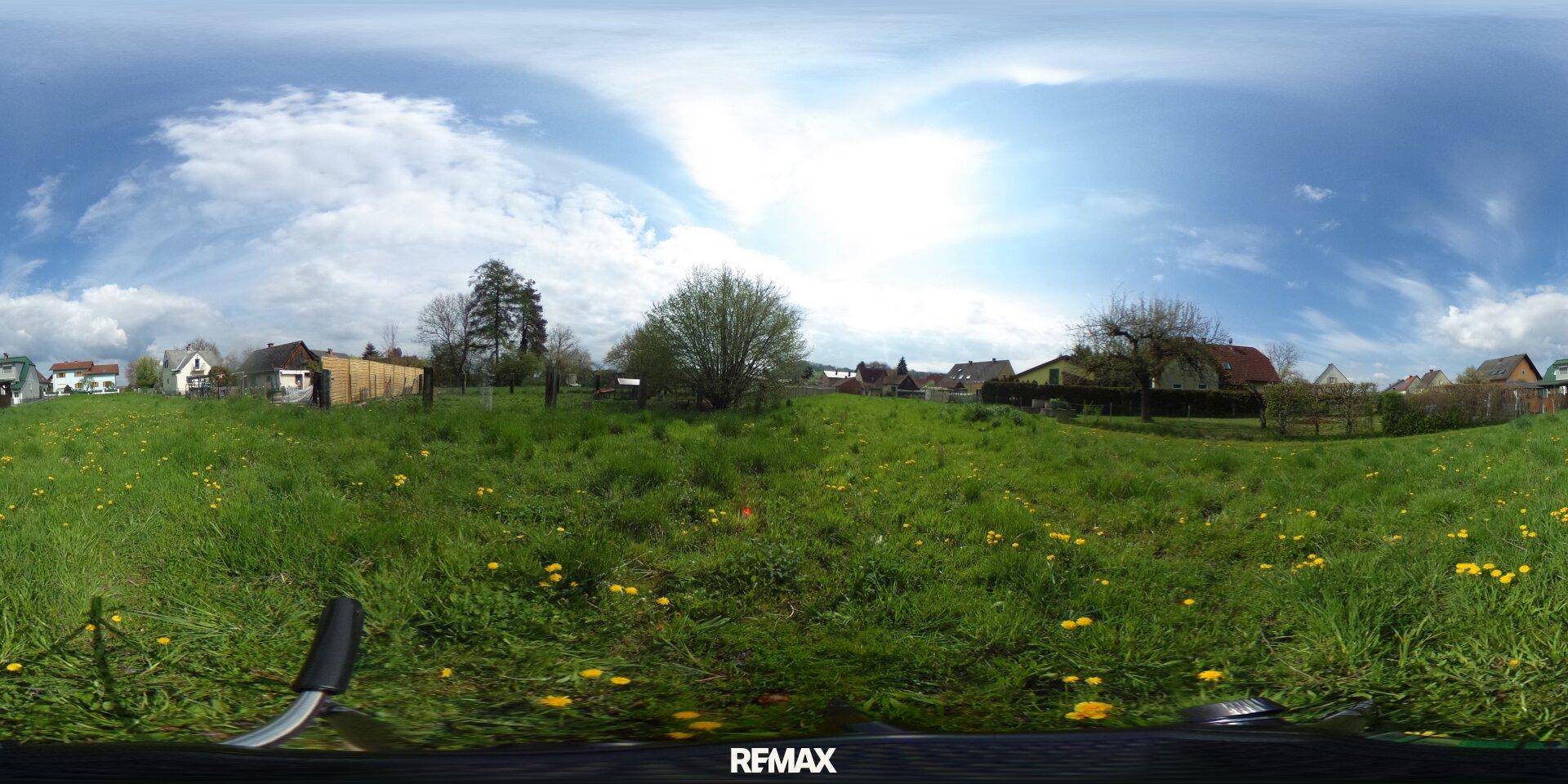 360-Grad-Panoramaansicht eines weitläufigen grünen Grundstücks mit umliegenden Häusern unter blauem Himmel.