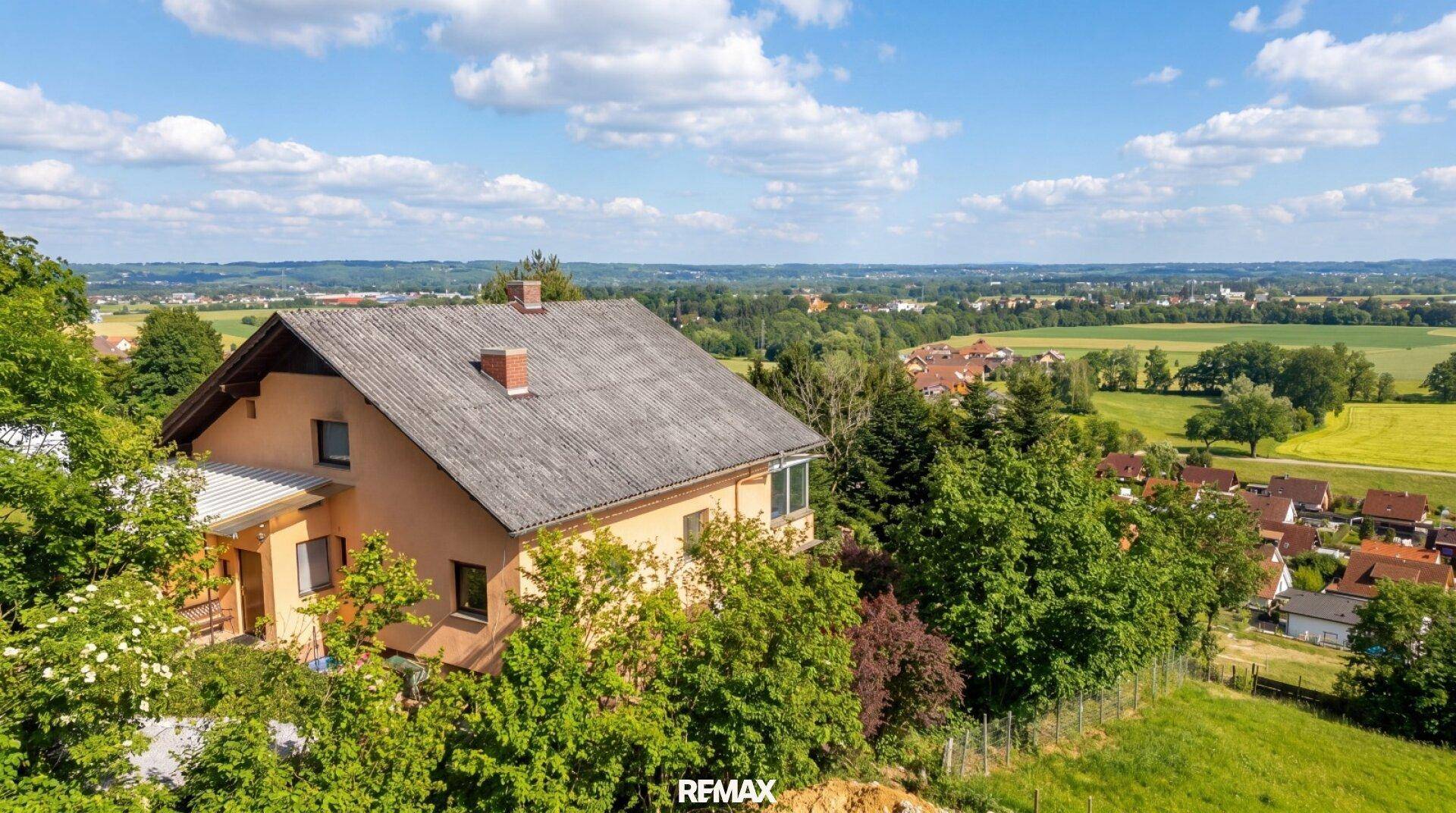 Ansicht eines Einfamilienhauses mit Satteldach, umgeben von Bäumen und weitem Blick über die Landschaft.