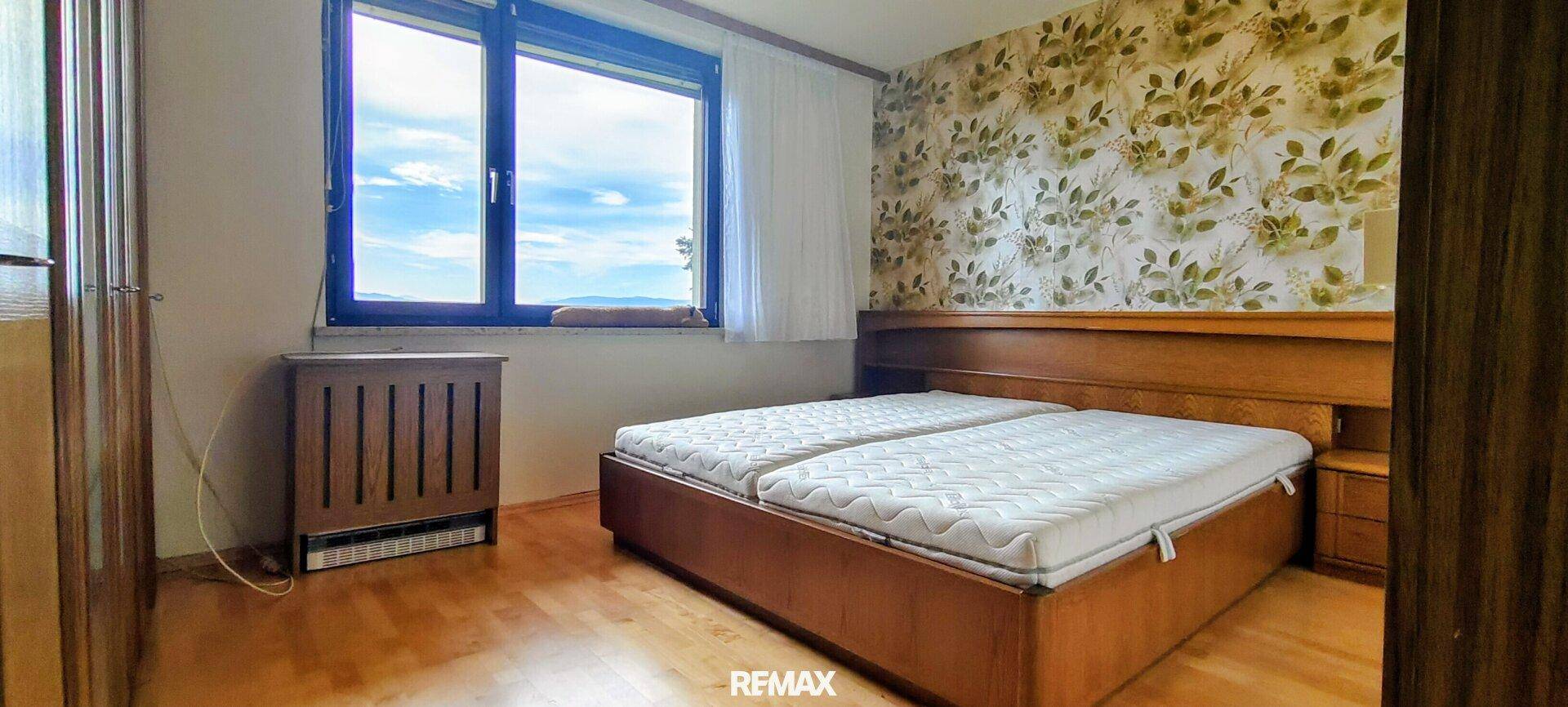 Schlafzimmer mit Doppelbett, Holzmöbeln und floraler Tapete, bietet einen weiten Ausblick.