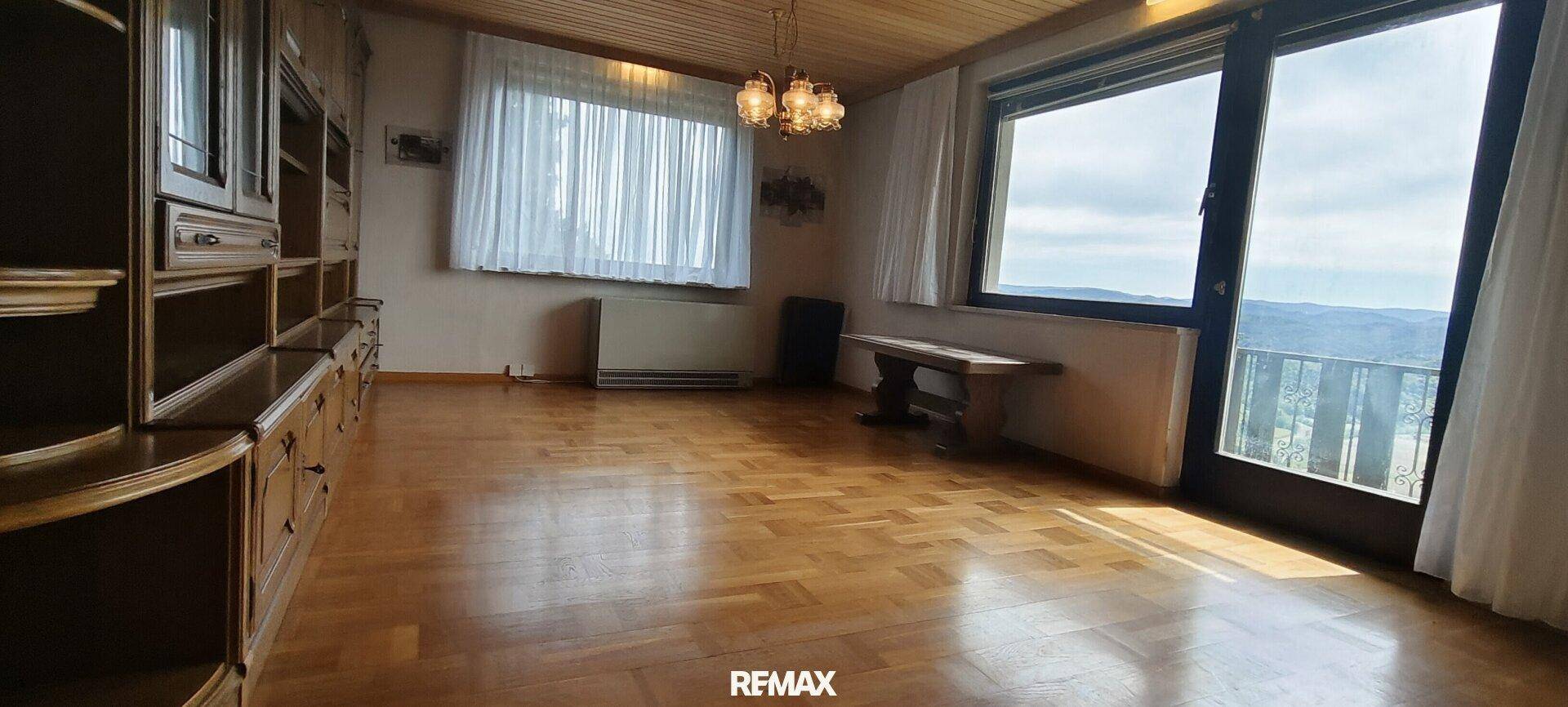 Geräumiges Wohnzimmer mit Parkettboden, Holzschrankwand und großen Fenstern mit Fernblick.