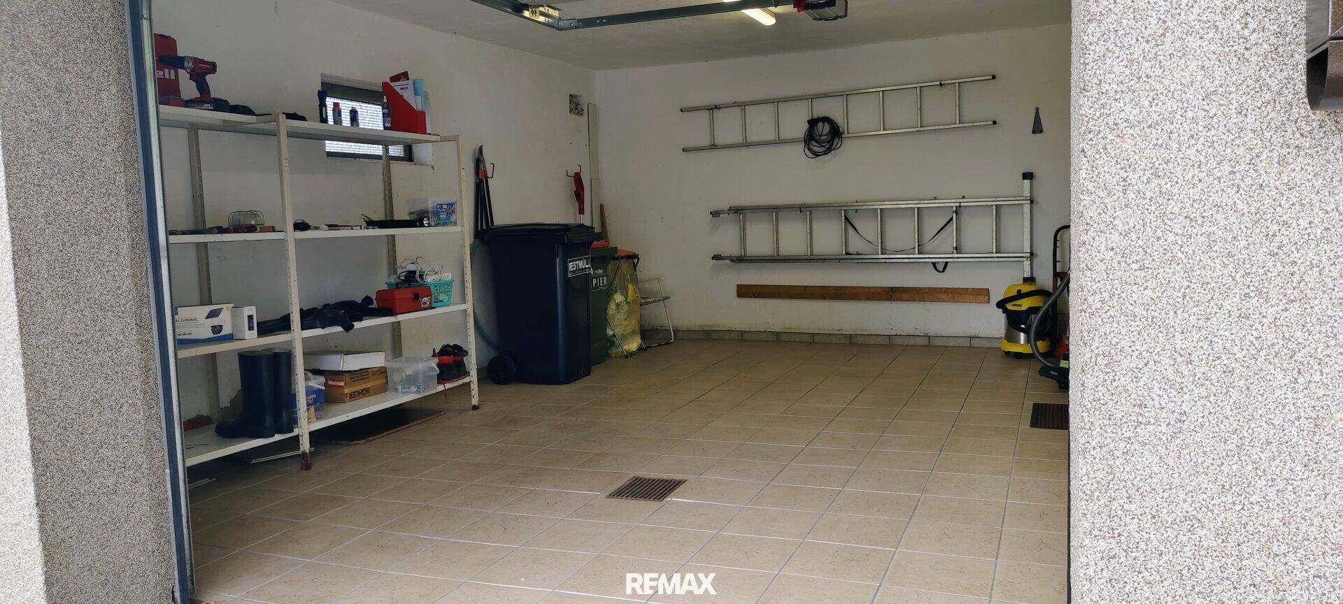 Geräumige Garage mit Fliesenboden, Regalen und Stauraum für Werkzeuge und Geräte.