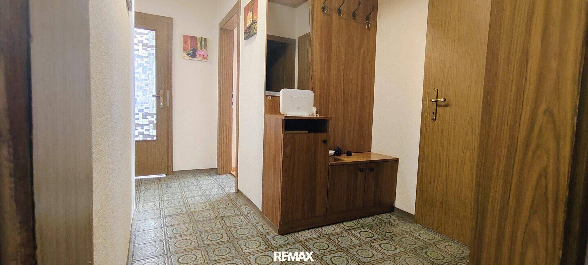Flur mit gemusterten Fliesen, Holzmöbeln und Garderobe, verbindet verschiedene Räume.