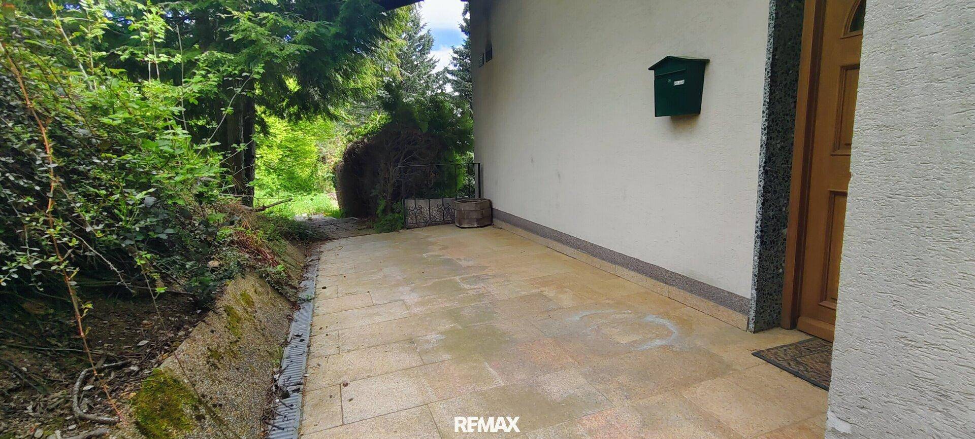 Gepflasterter Weg entlang der Hauswand mit Briefkasten und Zugang zum Garten.