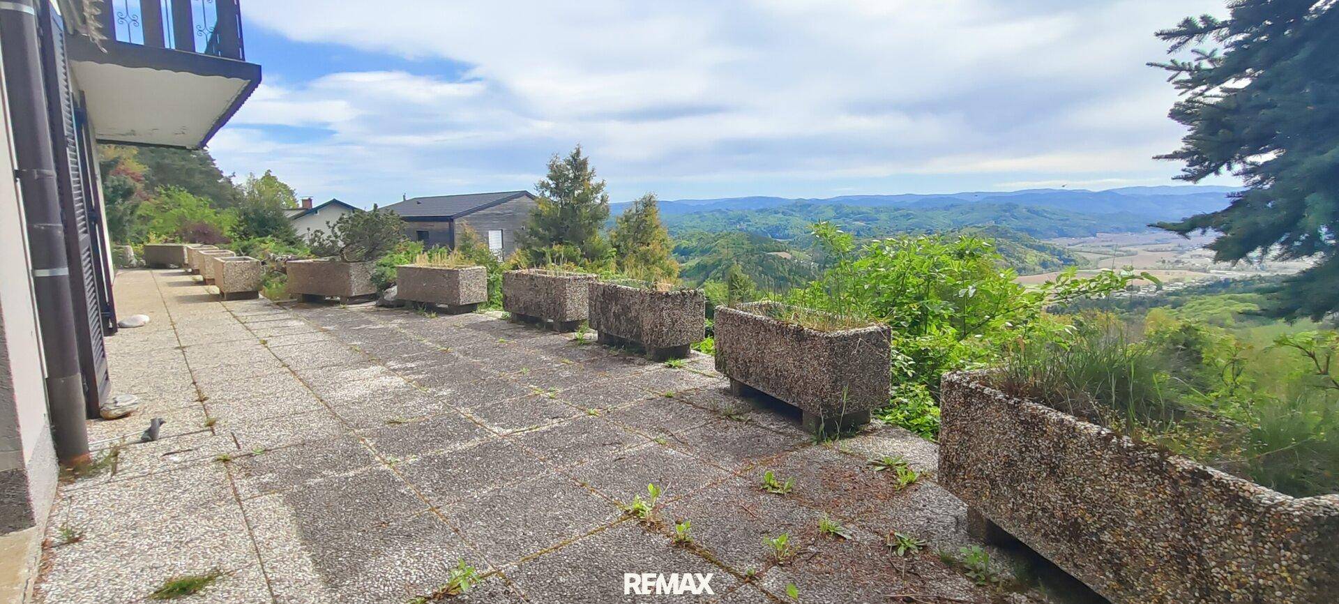 Große Steinterrasse mit Pflanzkübeln und weitem Blick über die hügelige Landschaft.