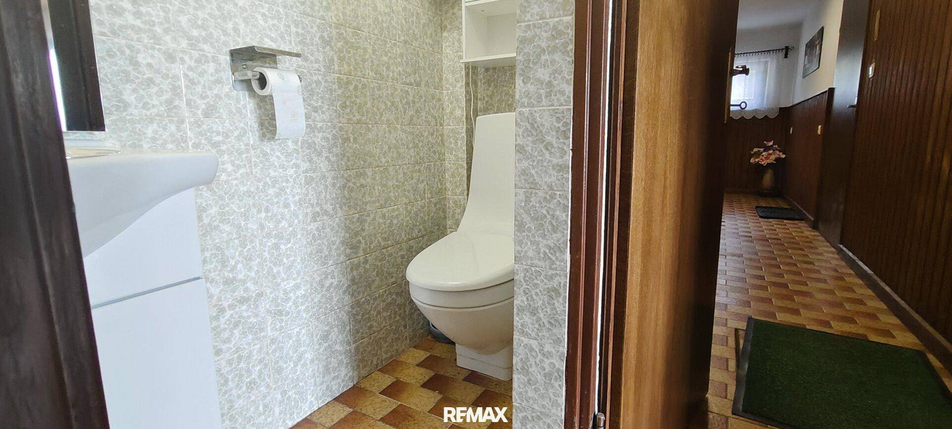 Kleines WC mit Wandfliesen, Toilette und Waschbecken, funktional eingerichtet.