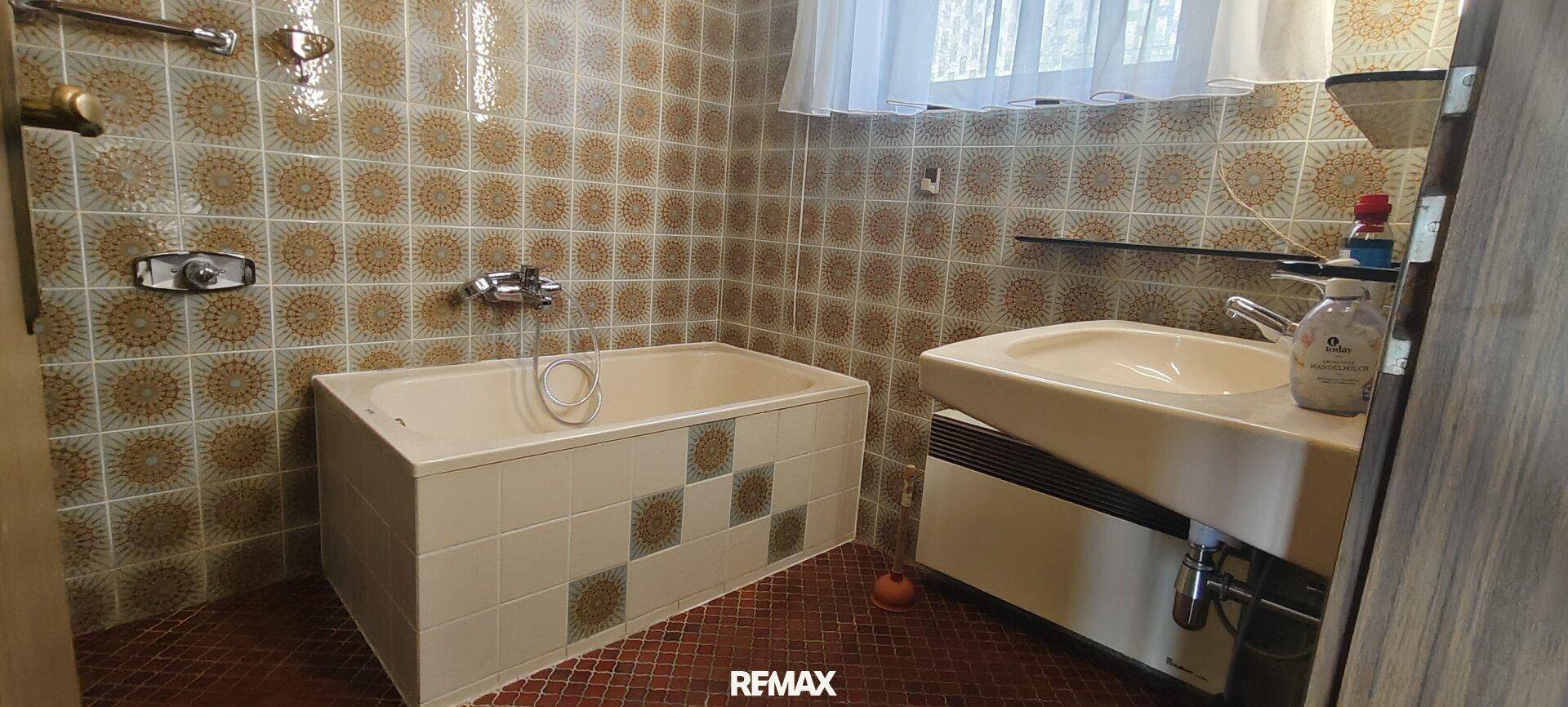 Badezimmer mit Badewanne, Waschbecken und gemusterten Fliesen im Retro-Stil.