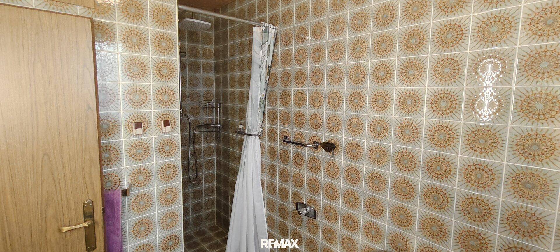 Duschbereich im Badezimmer mit gemusterten Fliesen und Duschvorhang.