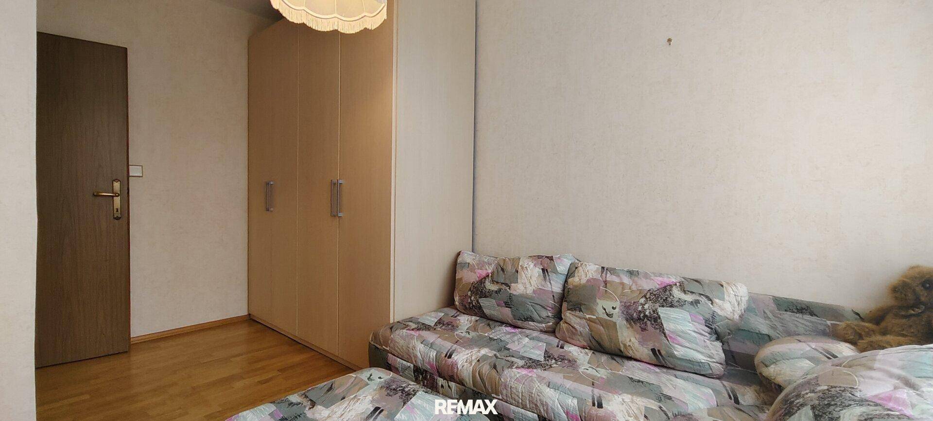 Einfaches Zimmer mit Sofa, Kleiderschrank und schlichten Wänden, ideal als Gästezimmer.