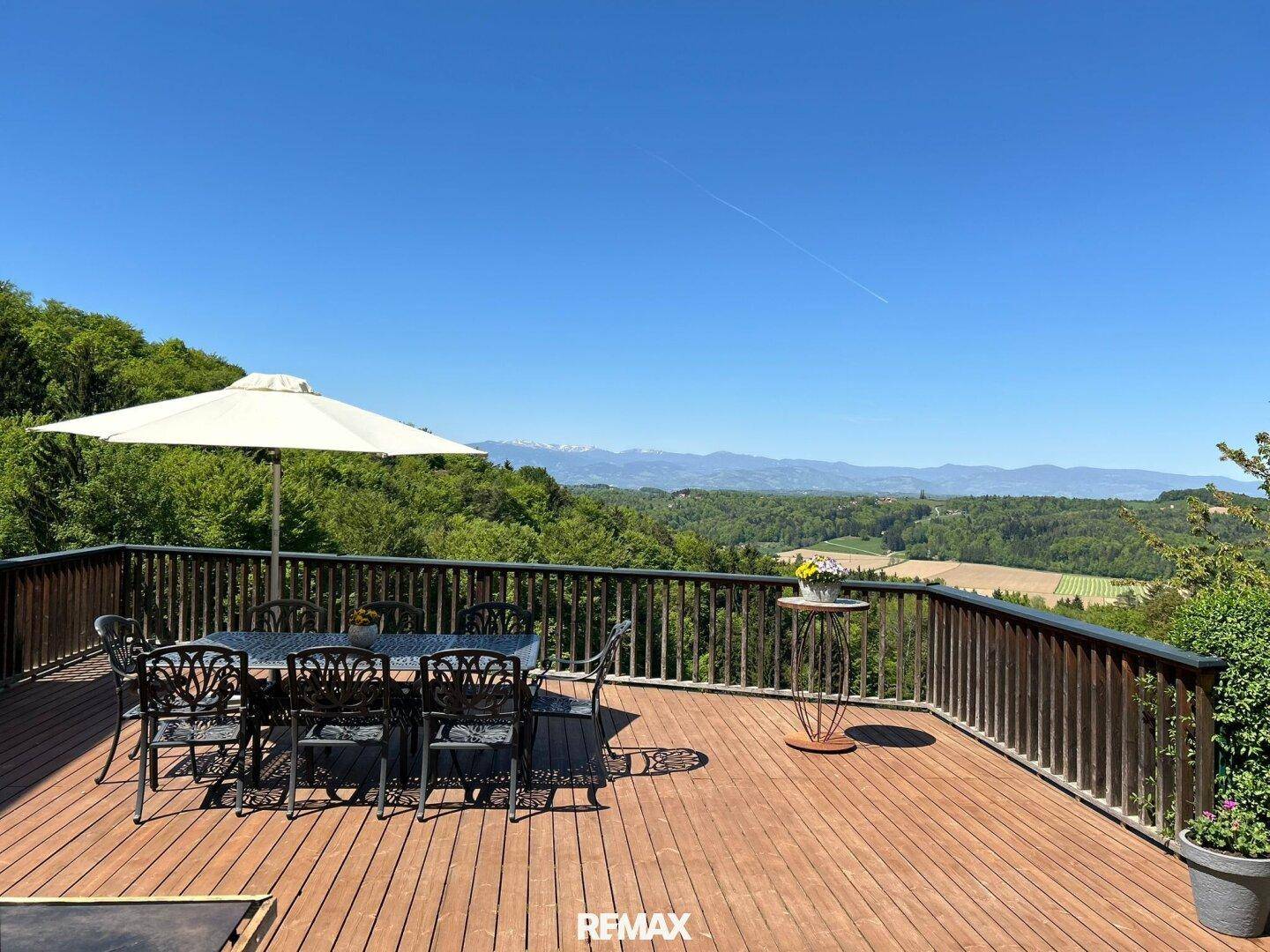 Große Holzterrasse mit Esstisch, Sonnenschirm und weitem Blick auf die Berge und Landschaft.