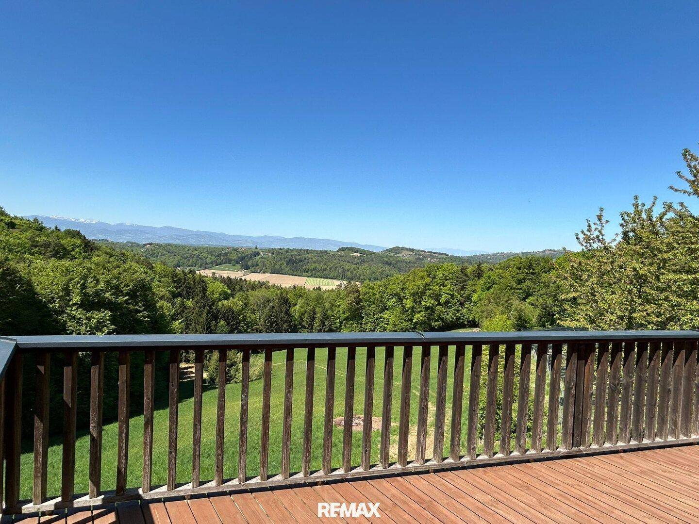 Panoramablick von der Holzterrasse über die grüne Landschaft und ferne Berge.