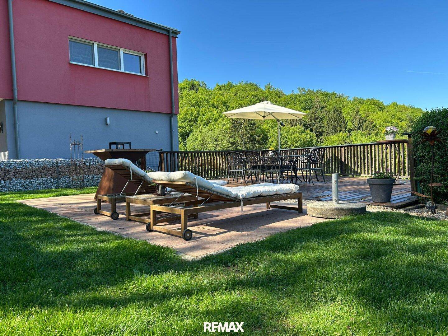 Gepflegter Gartenbereich mit Rasen, Sonnenliegen und einer Holzterrasse am Haus.