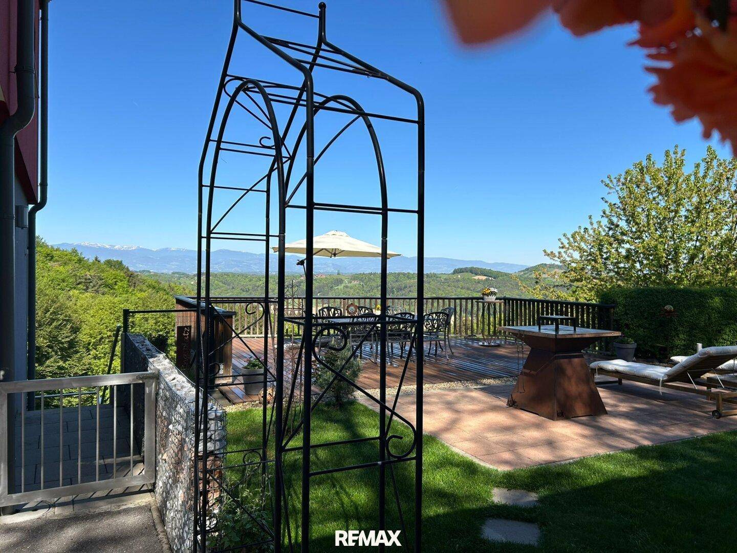 Gartenbereich mit Rasen, Terrasse und einem dekorativen Metallbogen im Vordergrund.