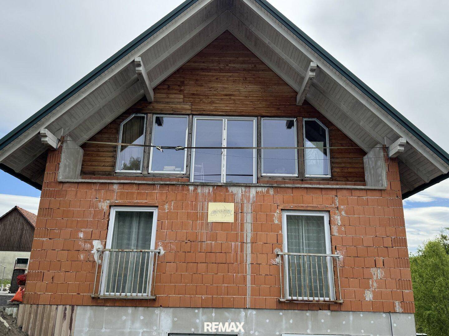 Giebelansicht des Hauses mit Holzverkleidung, großen Fenstern und französischen Balkonen im Obergeschoss.