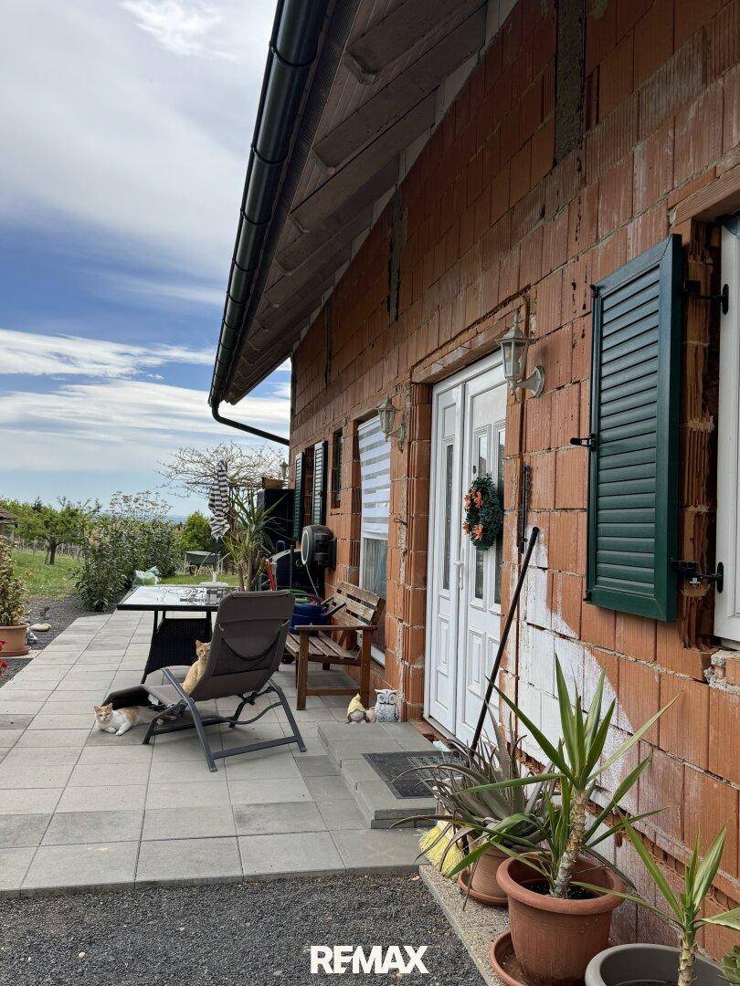 Gemütliche Terrasse am Haus mit Sitzgelegenheiten, Pflanzen und Blick auf die umliegende Landschaft.