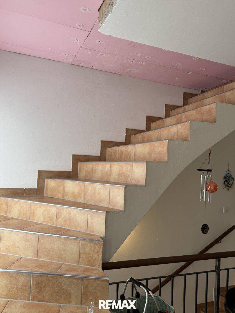 Geflieste Treppe mit Metallgeländer, die in ein noch nicht fertiggestelltes Obergeschoss führt.