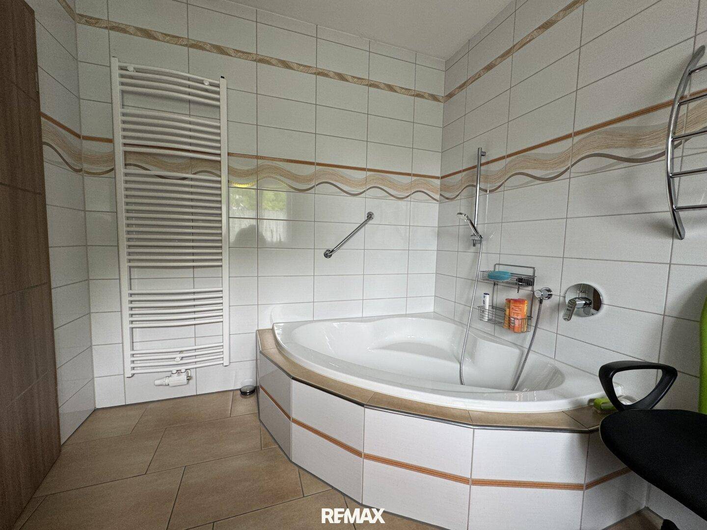 Gefliestes Badezimmer mit Eckbadewanne, Handtuchheizkörper und praktischen Haltegriffen.