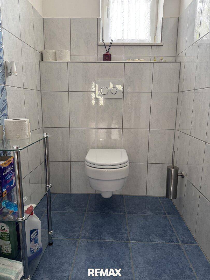 Modernes WC mit Wand-WC, blauen Bodenfliesen und einem Fenster für natürliche Belüftung.