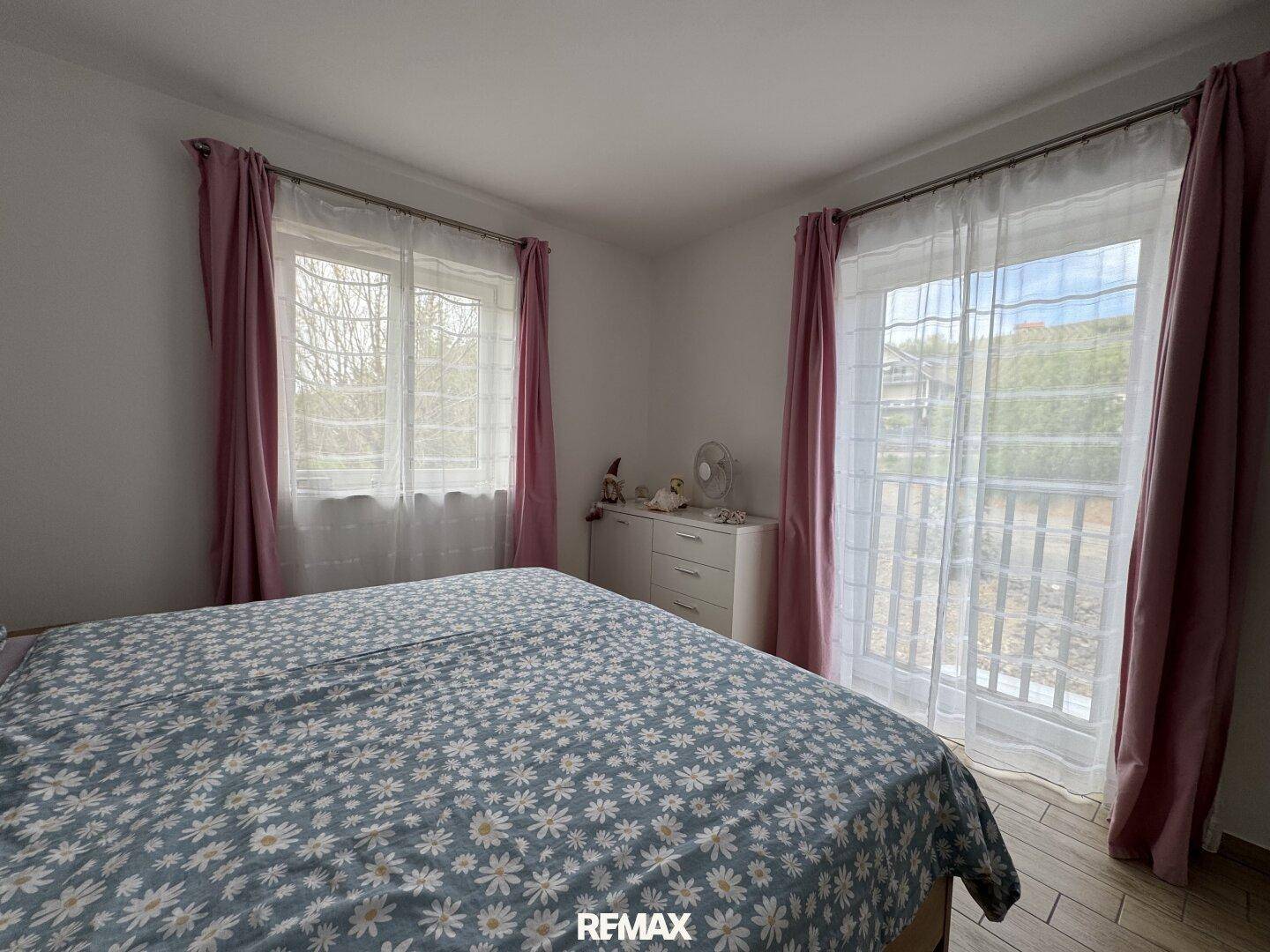 Helles Schlafzimmer mit Doppelbett, Laminatboden und Zugang zu einem französischen Balkon.