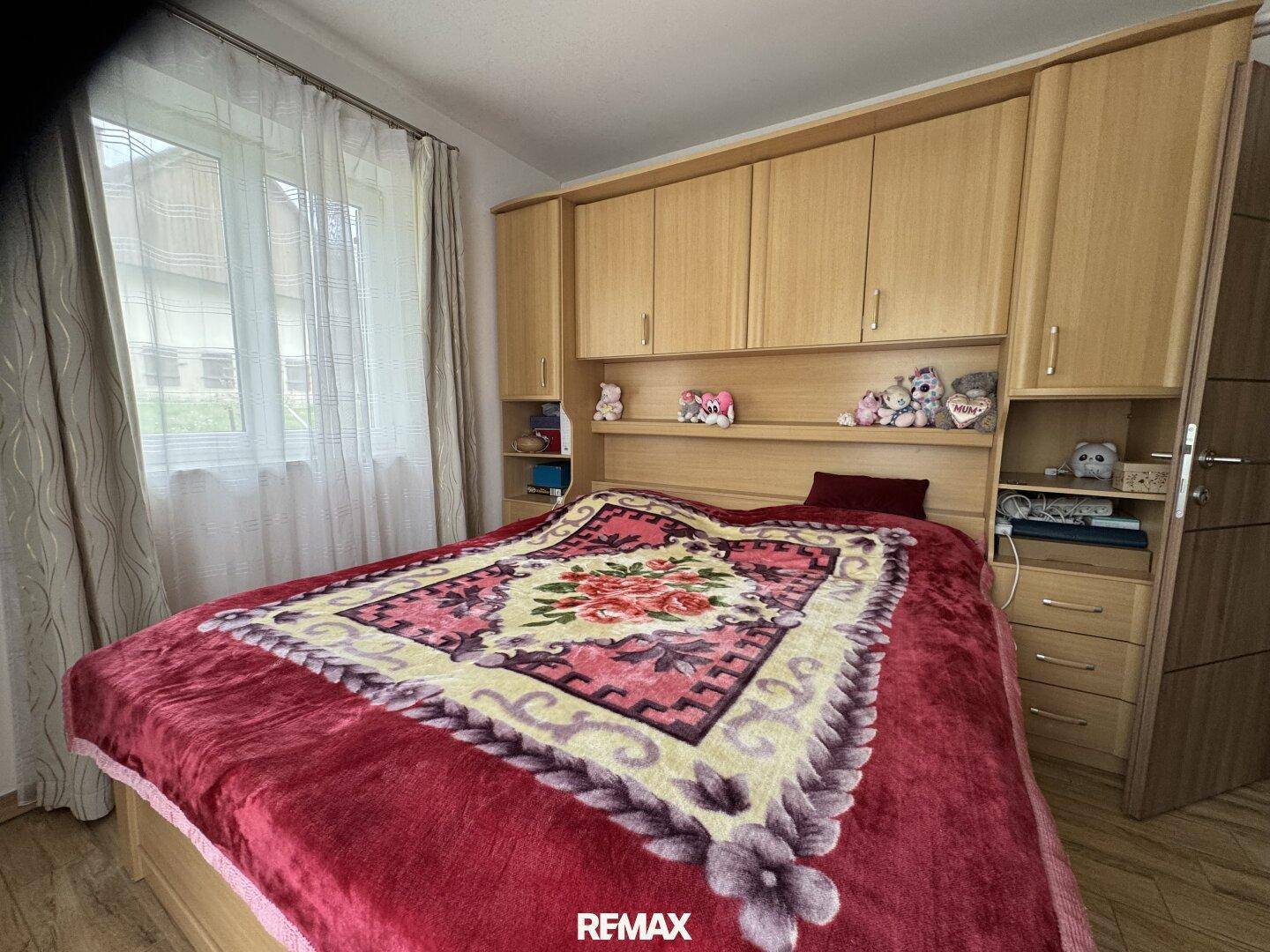 Schlafzimmer mit Einbauschränken über dem Bett, Laminatboden und einem großen Fenster.