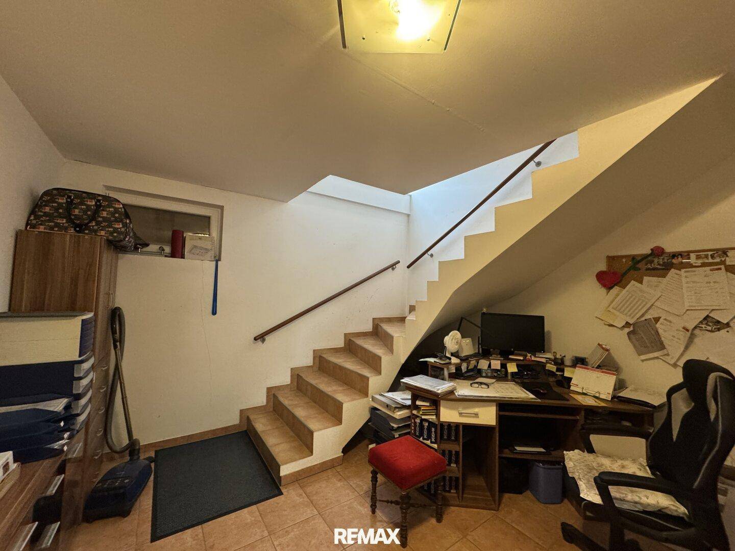 Kellerraum, der als Büro genutzt wird, mit Schreibtisch, Stuhl und Zugang zur Treppe.