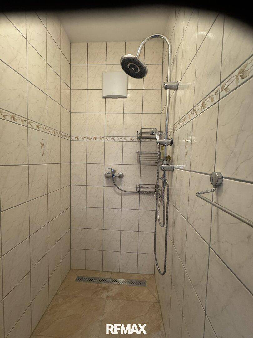 Geflieste Duschkabine mit Duschkopf und Handbrause in hellem Design.