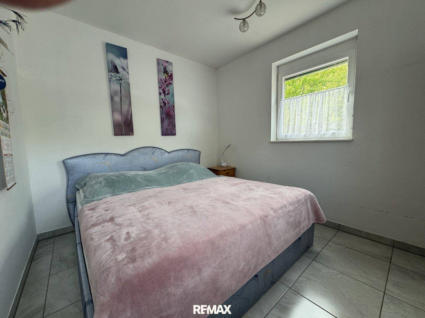 Schlafzimmer mit Doppelbett, Fliesenboden und Fenster mit Blick ins Grüne.
