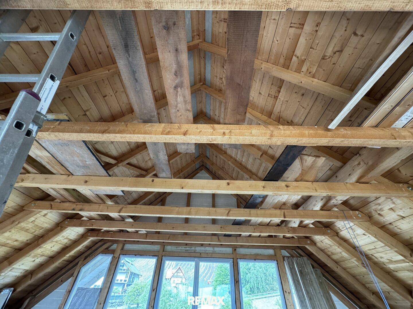 Unfertiger Dachboden mit sichtbaren Holzbalken und Fenstern, bereit für Ausbau.