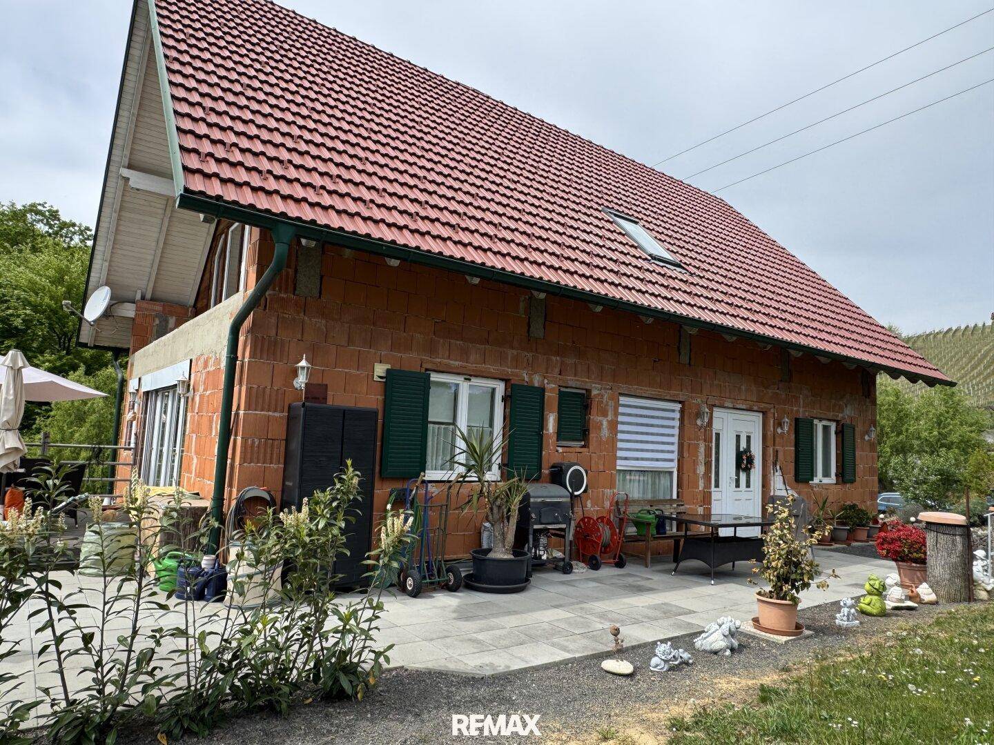 Seitenansicht des Hauses mit rotem Ziegeldach, Ziegelmauerwerk und einer Terrasse mit Blick ins Grüne.